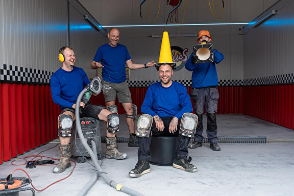 Vrolijk personeel in een wasbox waar ze een vloer aan het leggen zijn.