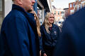 Een blonde vrouw in een donkerblauwe jas staat lachend tussen andere mensen op straat; de mensen op de voorgrond zijn onscherp.